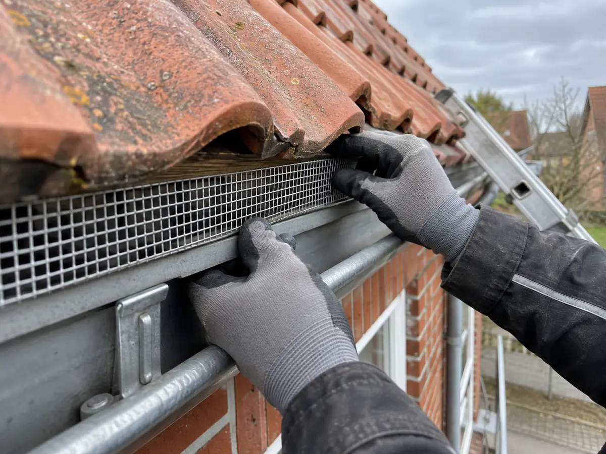 Handwerker verschließt die Traufe eines Klinkerhauses mit einem Metallgitter